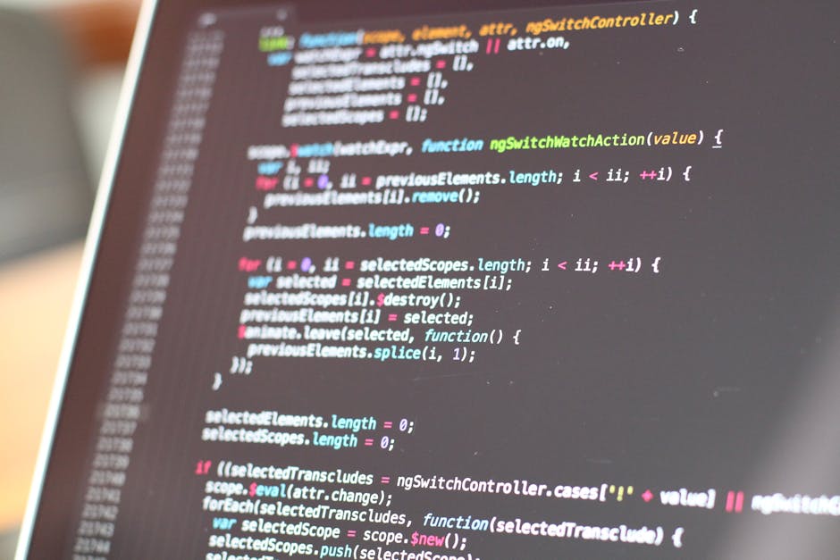 A close-up photograph of a computer screen displaying lines of colourful programming code with syntax highlighting in shades of blue, pink, green, and white on a dark background. The screen is slightl